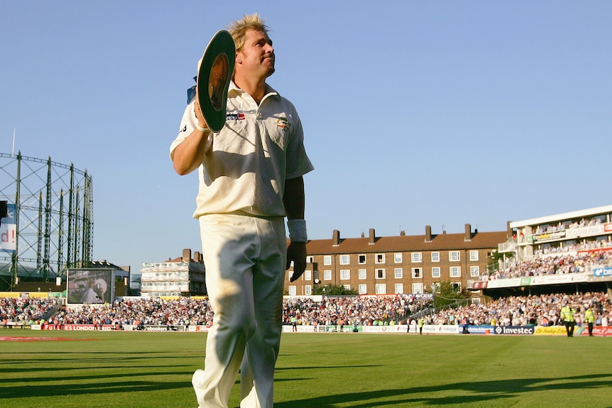 A man holds a wide brimmed hat in his hand and acknowledges the crowd