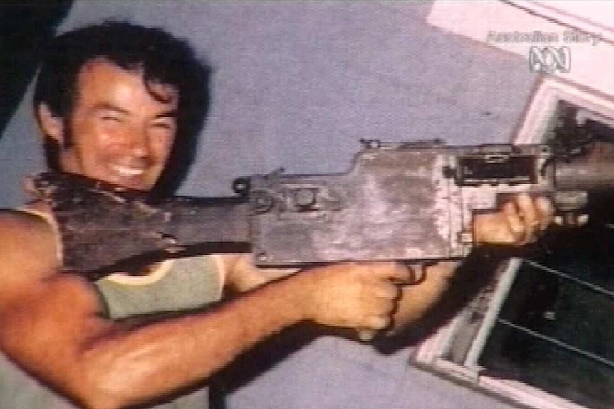 A smiling man holds a large gun.