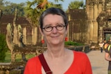 A woman with short hair wearing a red shirt posing for a photo in front of temple ruins