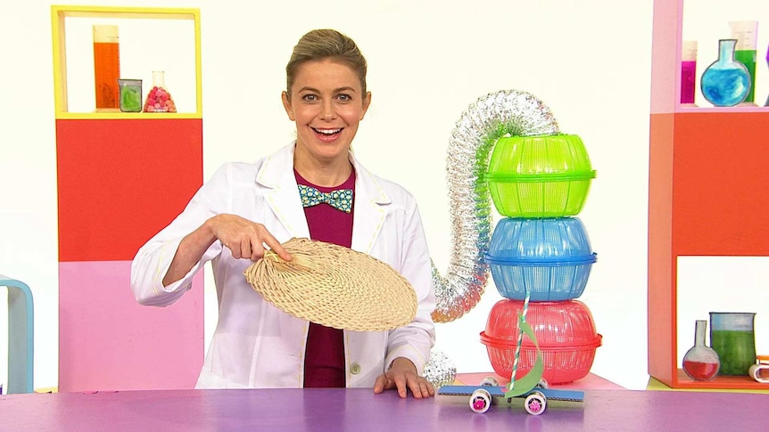 Rachael on the Play School Science Time set wearing a lab coat holding a fan with her craft car