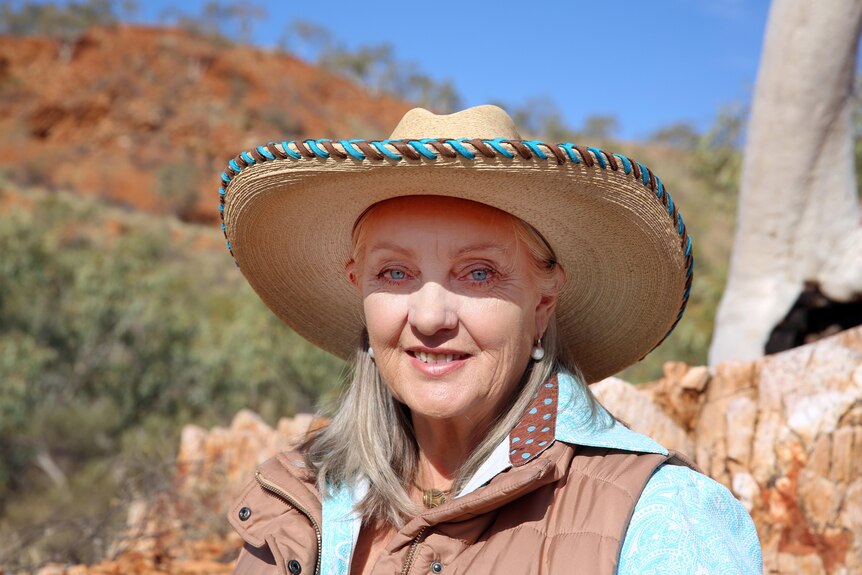 A middle aged woman in a rural area, with bright blue eyes wearing a hat. 