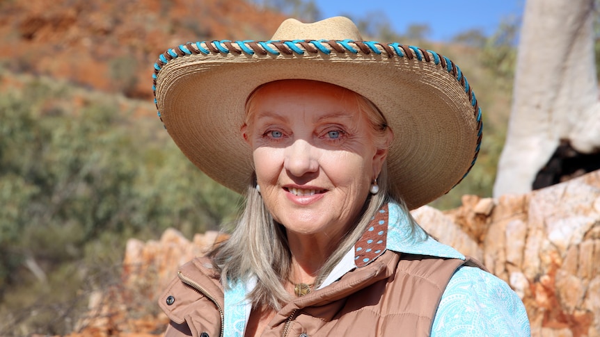 A middle aged woman in a rural area, with bright blue eyes wearing a hat. 