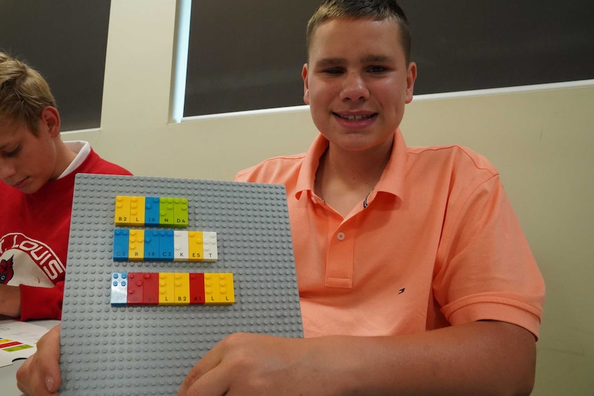 Ollie holds up a board with an arrangement of Lego Braille Bricks.