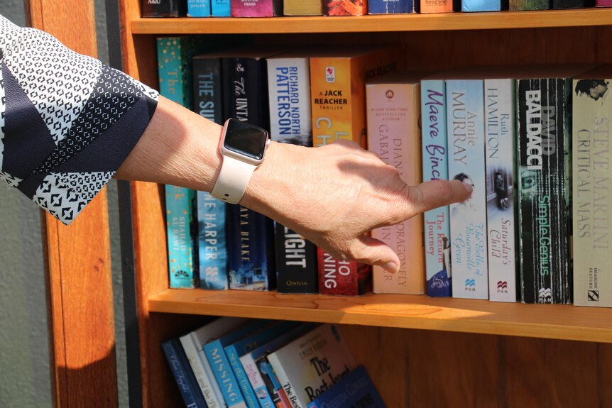 The hand of a woman wearing a watch as she points at books on a shelf