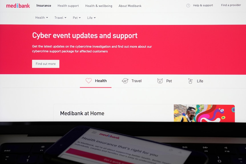 A phone showing the Medibank page sits on a laptop open to Medibank's website. 