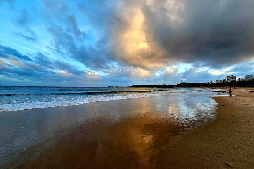 a swimmer standing on the sand at Mooloolaba Beach in Queensland as the sky is covered in dark menacing clouds