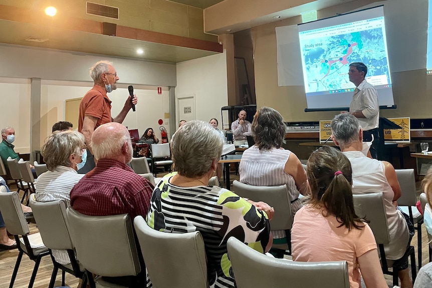 An older man speaks from the crowd at a community meeting.