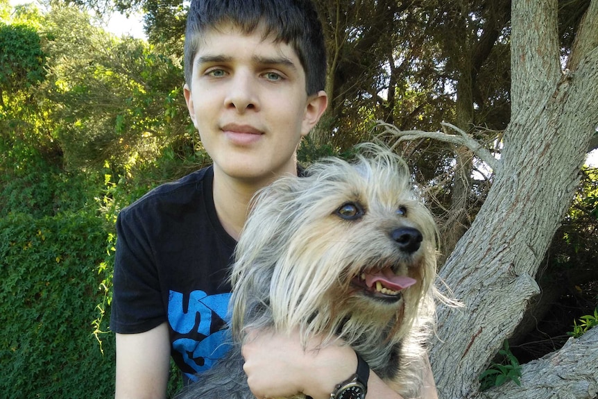 A teenage boy holds a small dog.