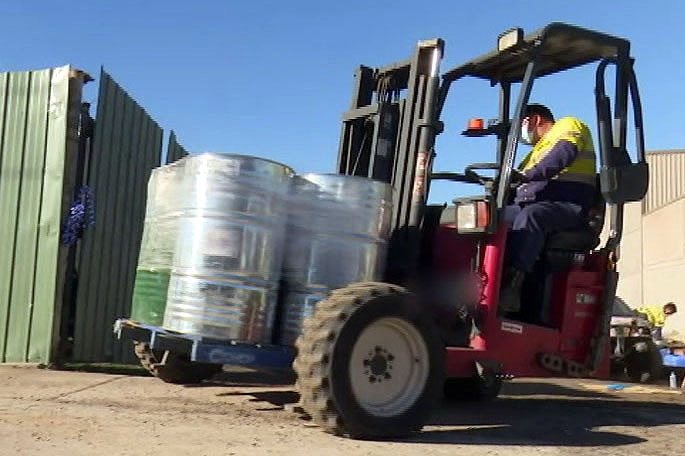 A worker driving a forklift with several drums of GHB chemicals.