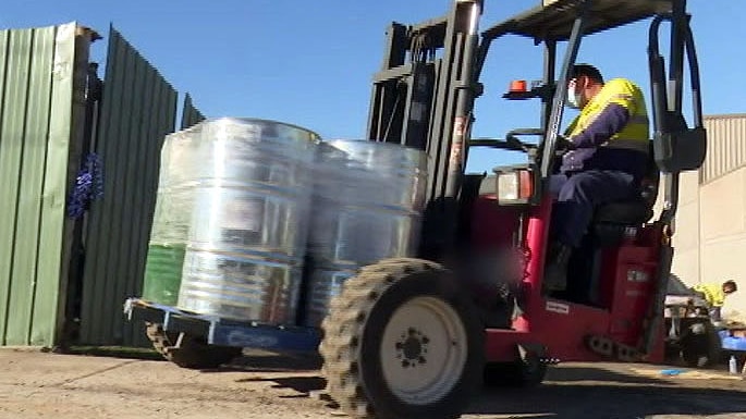 A worker driving a forklift with several drums of GHB chemicals.