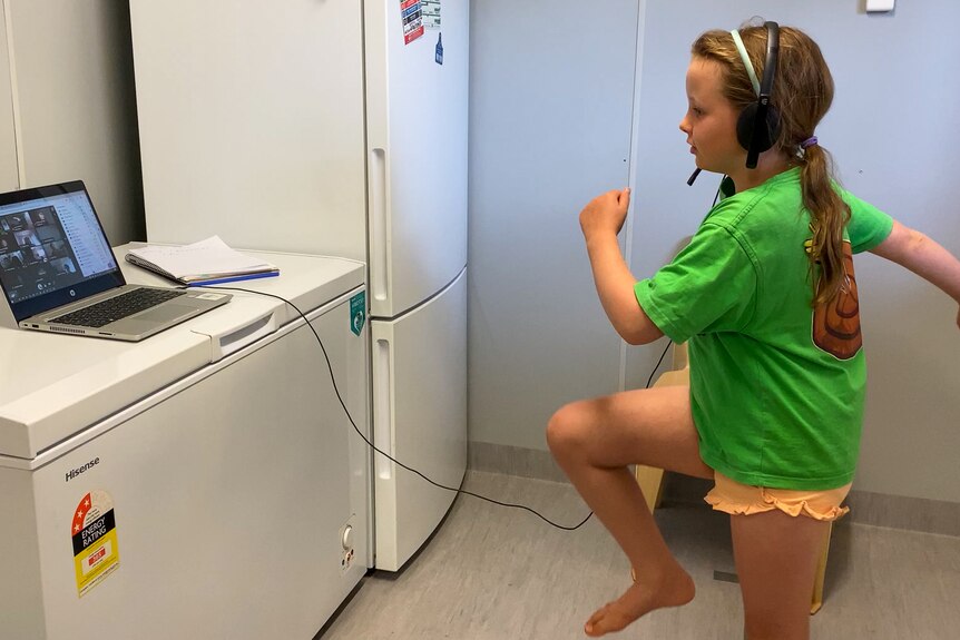 A young girl dances in front of a computer sitting on a chest freezer, near Longreach, November 2022.