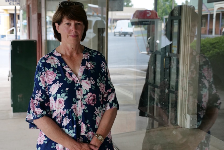 Woman in floral dress looks somber, pictured next to empty shop front on main street.