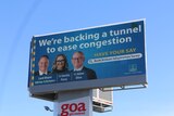 An image of a blue billboard featuring three people and the words 'We're backing a tunnel to ease congestion'.