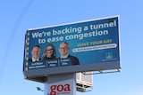 An image of a blue billboard featuring three people and the words 'We're backing a tunnel to ease congestion'.