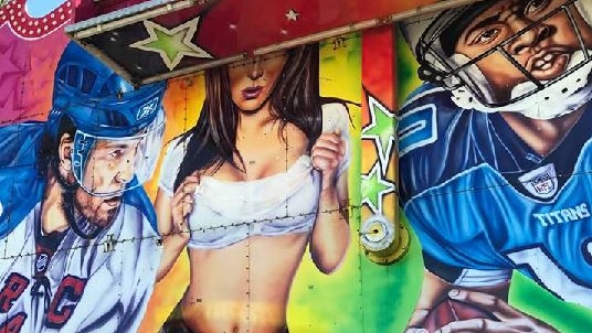 Mural depicting woman in midriff top, shorts and suspenders, surrounded by footballers