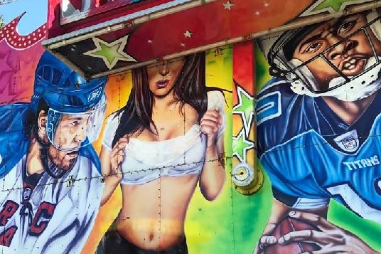 Mural depicting woman in midriff top, shorts and suspenders, surrounded by footballers