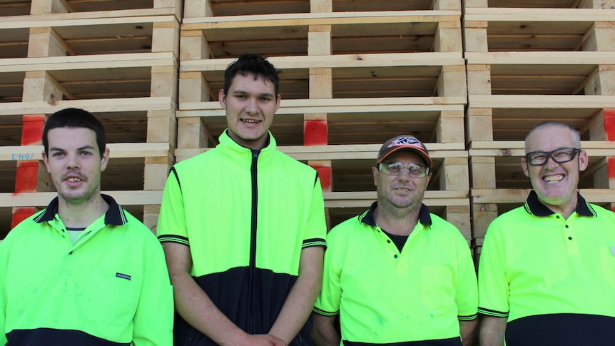 A group of Gumnut Place supported employees stand in front of stacks of pallets waiting to be heat treated.