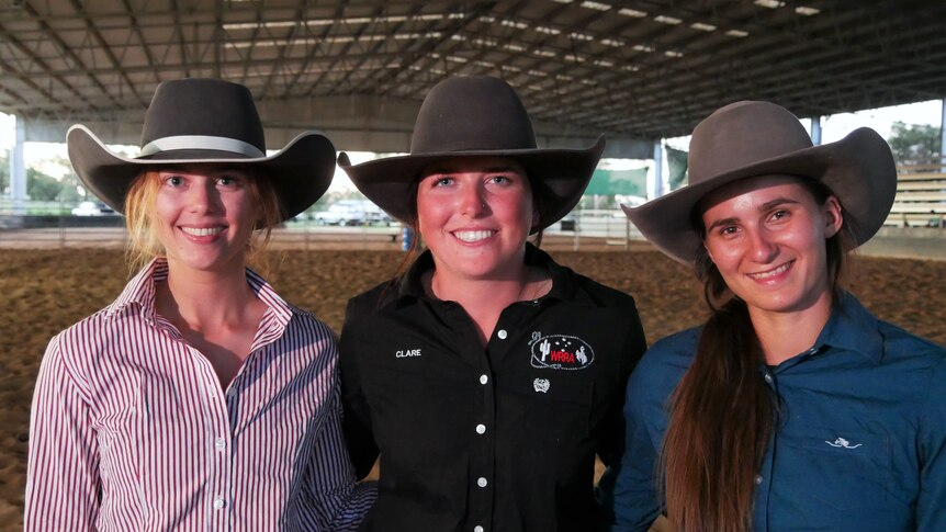 Three women in button up shirts with large hats on. 