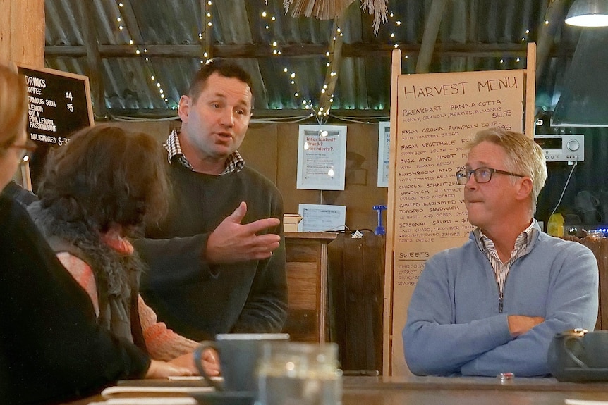 Don Elgin sits at the head of a table in a rustic restaurant speaking to a small group, including Phil Hayes-Brown.