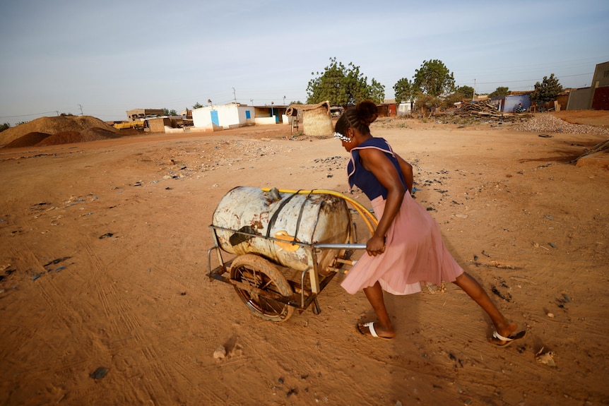 A woman pushes a barrel filled with water on the outskirts of Ouagadougou, Burkina Faso.