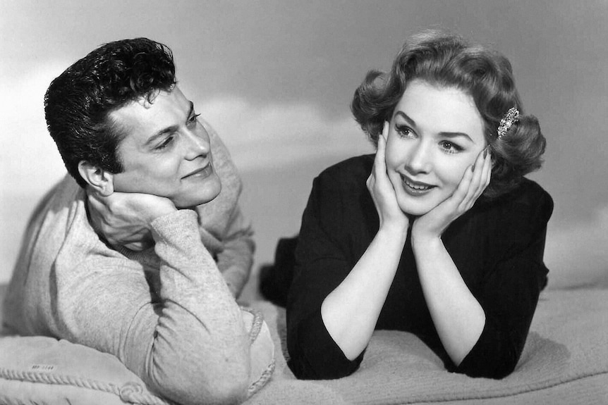 Tony Curtis and Piper Laurie lay next to each other in a black and white movie publicity shoot. 