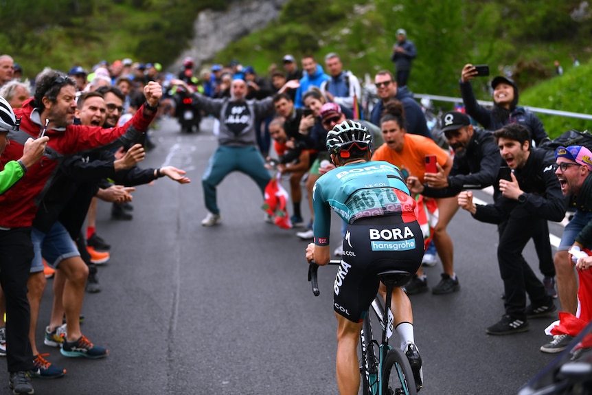 El ciclista australiano Jai Hindley sube la cuesta por su cuenta, mientras los fanáticos invaden el camino por el que ruge. 