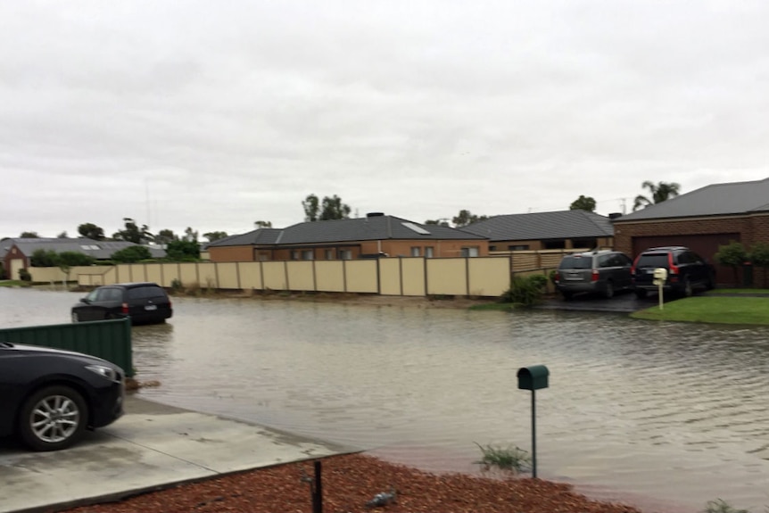 A car drives through floodwaters which have rendered the road line markings invisible.