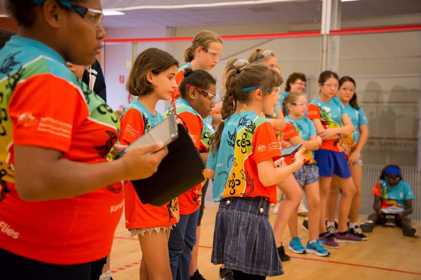 A line of girls aged between 10 and 17 focus intently on the small drones they are flying with tablet-style controllers.