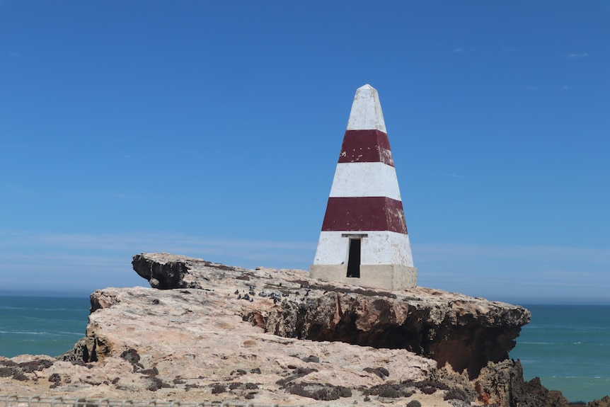 Un obelisco rojo y blanco en forma de pirámide al borde de un acantilado rocoso.