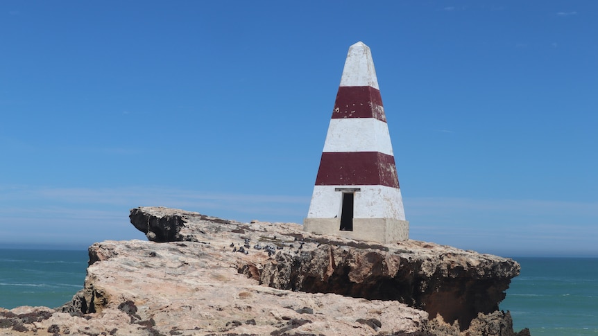 A red and white pyramid-shaped obelisk on the edge of a rocky cliff.