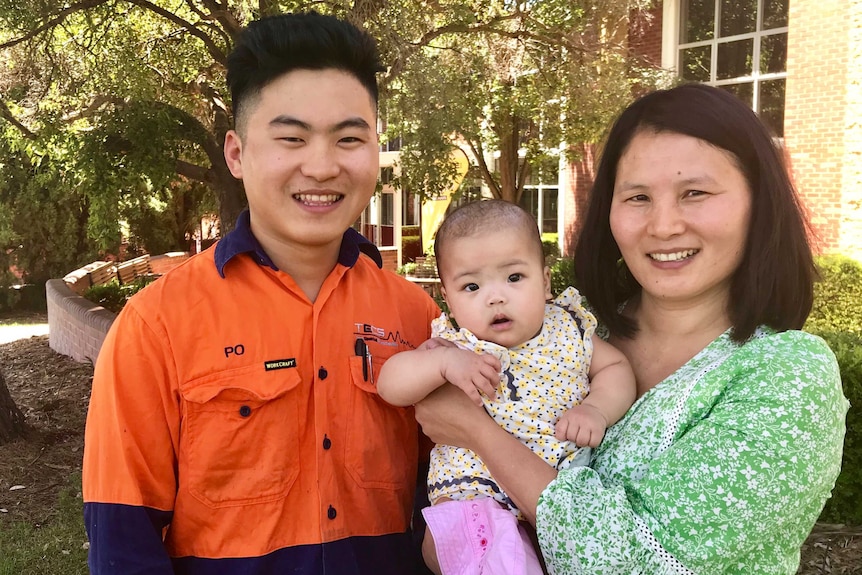 Burmese refugee and TAFE student smiling with his mother and infant sister