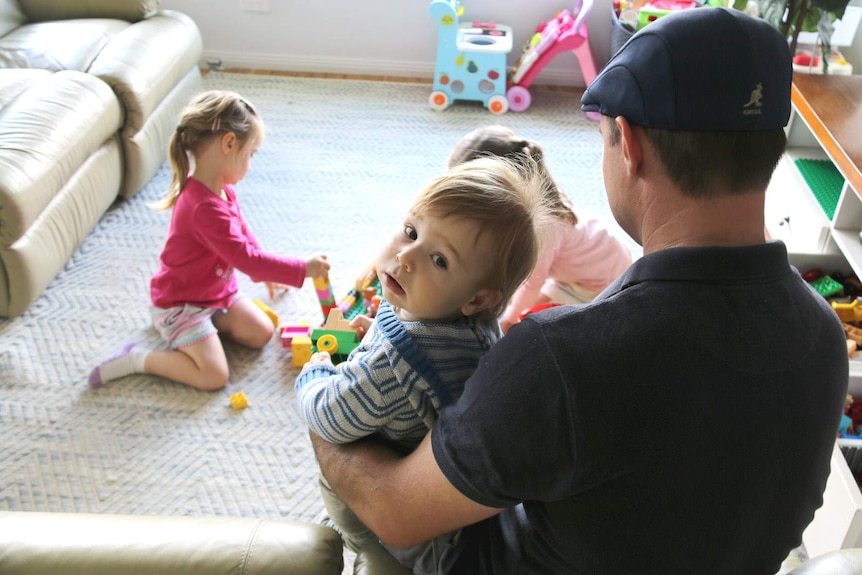 A dad plays with his small children in the family lounge room