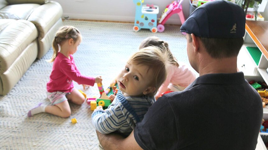 A dad plays with his small children in the family lounge room