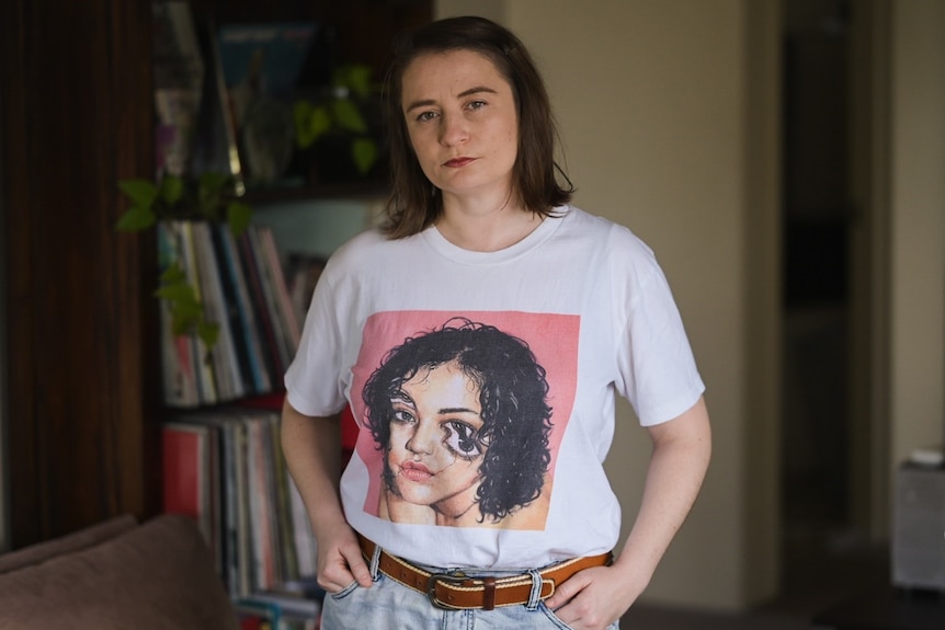 Une femme avec un t-shirt avec un visage déformé fait face à la caméra.