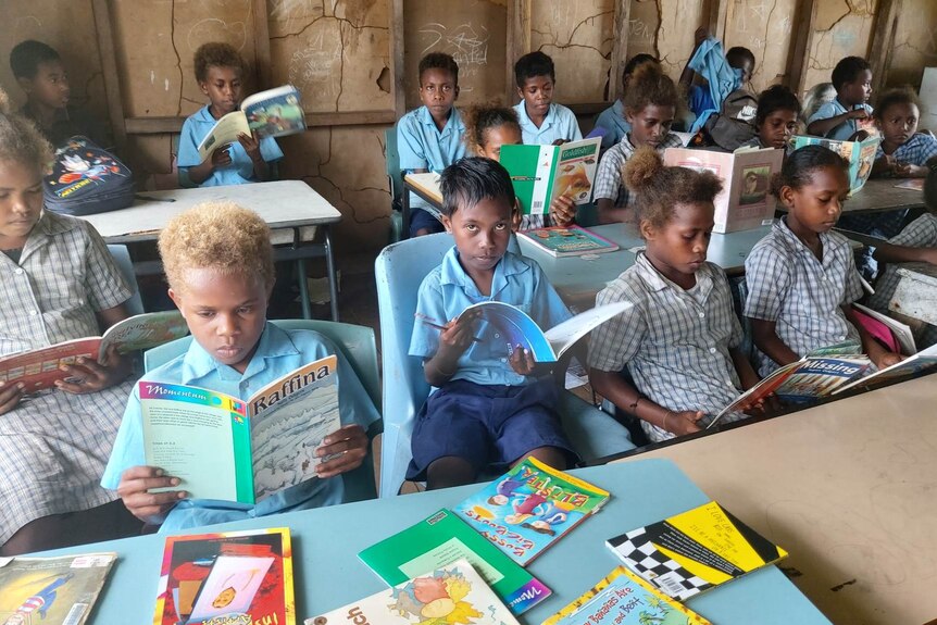  A group of children sitting in a classroom reading books.