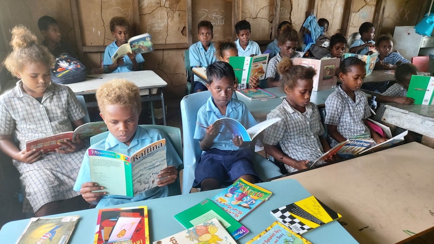  A group of children sitting in a classroom reading books.