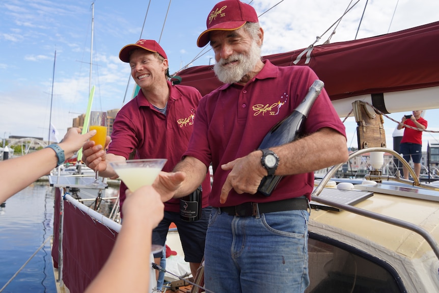 Two drinks are handed to two men on a yacht.