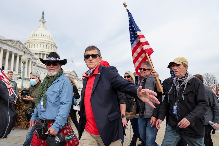 Michael Flynn gestures while walking with a crowd of people, one carrying a US flag, near Supreme Court and Capitol building 