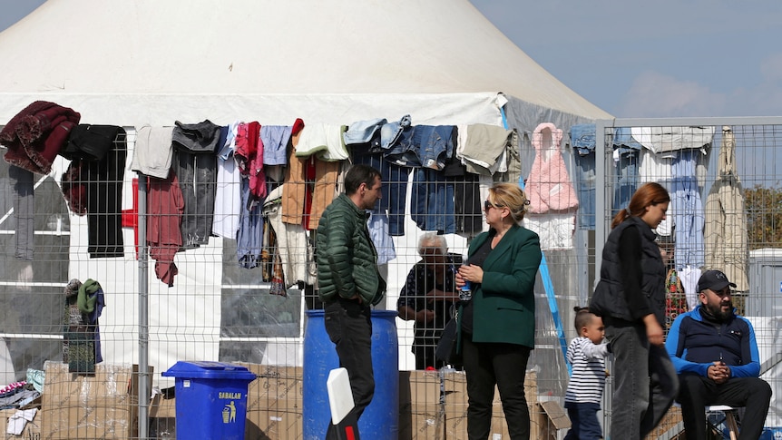 People standing in front of a fence with clothes haning on it. 