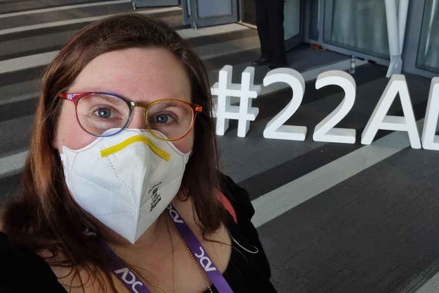 An image of Ash in a mask with the #22ADC letters on the ground behind her