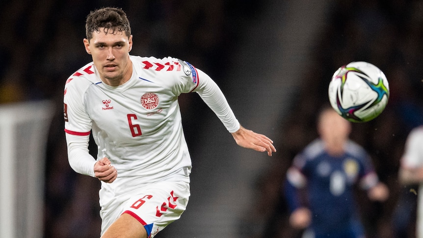 A Danish footballer runs forward with his eyes on the ball, as the Danish crest is visible on his shirt.