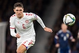 A Danish footballer runs forward with his eyes on the ball, as the Danish crest is visible on his shirt.