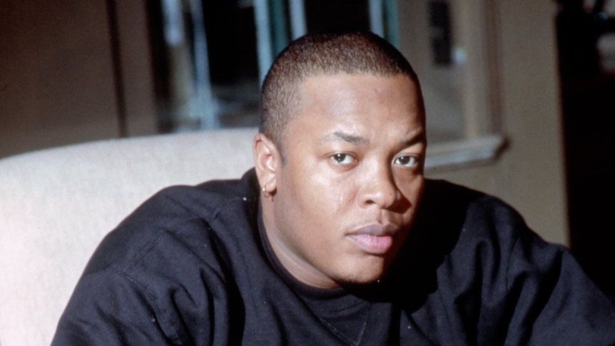Dr Dre sits a desk and looks at the camera