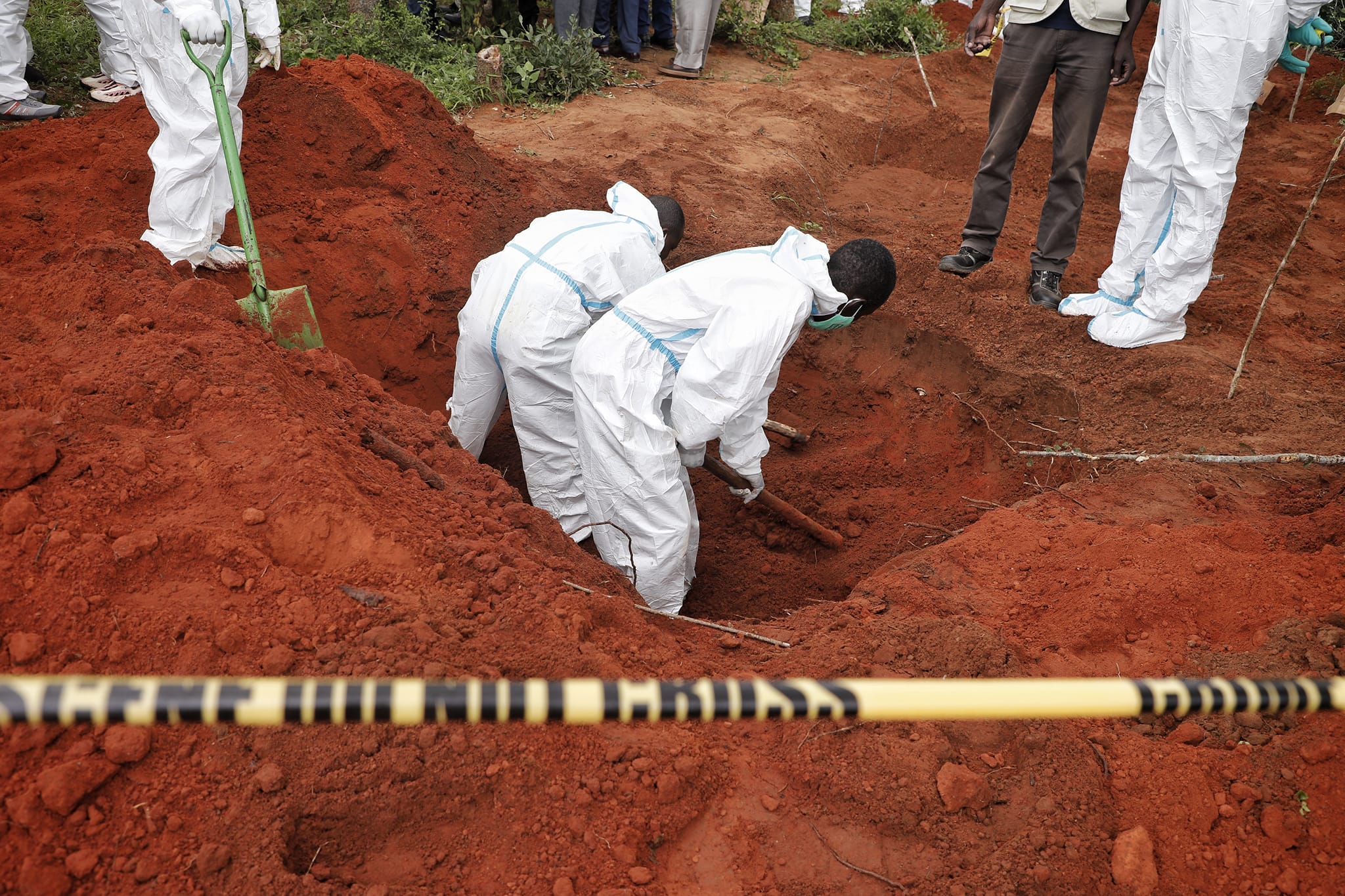 Forensic workers in white fully body suits dig into the red earth.
