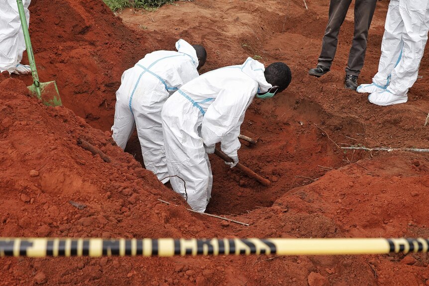 Forensic workers in white fully body suits dig into the red earth.
