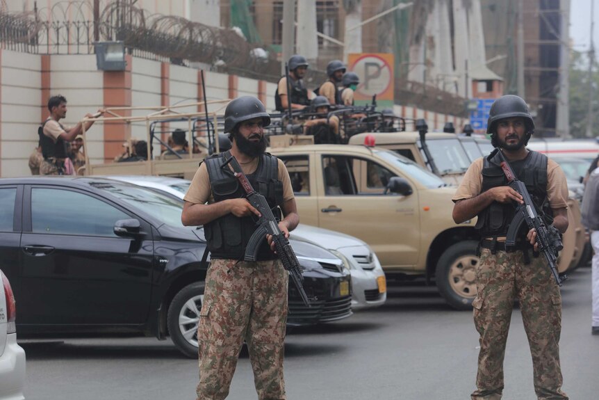 Men carrying automatic rifles and wearing bulletproof vests and helmets stand outside a walled complex.