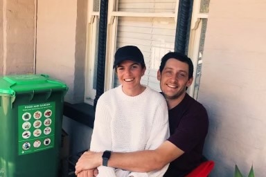 A young couple sit on their porch and smile at the camera.