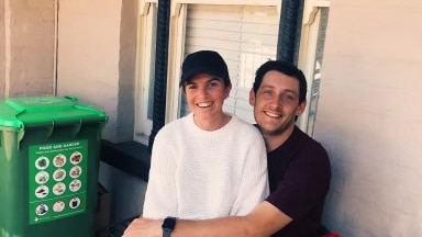 A young couple sit on their porch and smile at the camera.