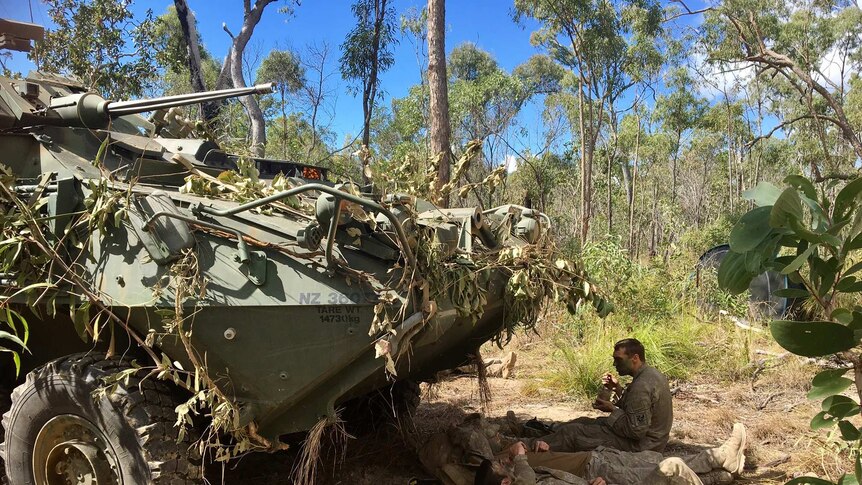Troops lay in the shade under a tank in bushland
