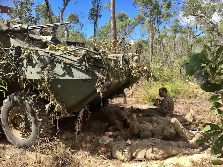 Troops lay in the shade under a tank in bushland